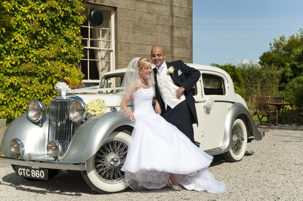 Bride beside a classic wedding car with ribbons